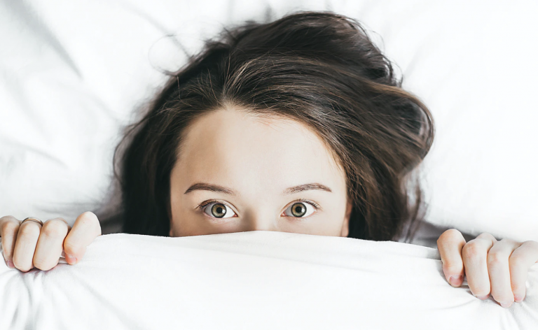A woman hiding underneath a blanket with half of her face showing.