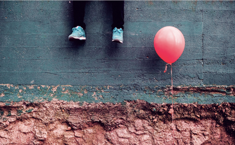 A pair of feet next to a red balloon.