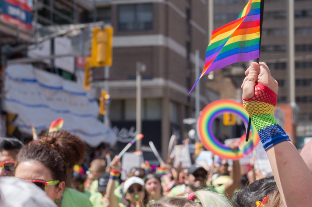 hand holding a pride flat aloft in the foreground of a pride parade, symbolising inclusivity