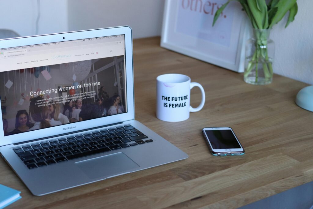 Lapton and mug on a wooden table. The laptop screen says "connecting women on the rise".