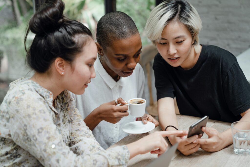 Three women looking at a phone together while the one in the middle holds a mug of coffee.