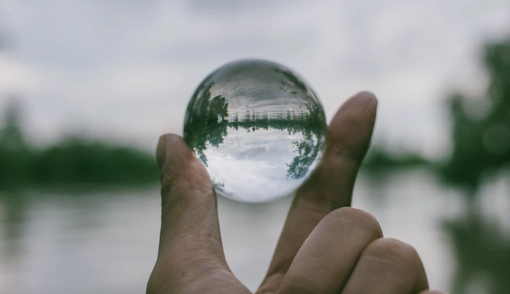 Hand holding a clear glass sphere with a serene landscape reflected inside, symbolizing transparency